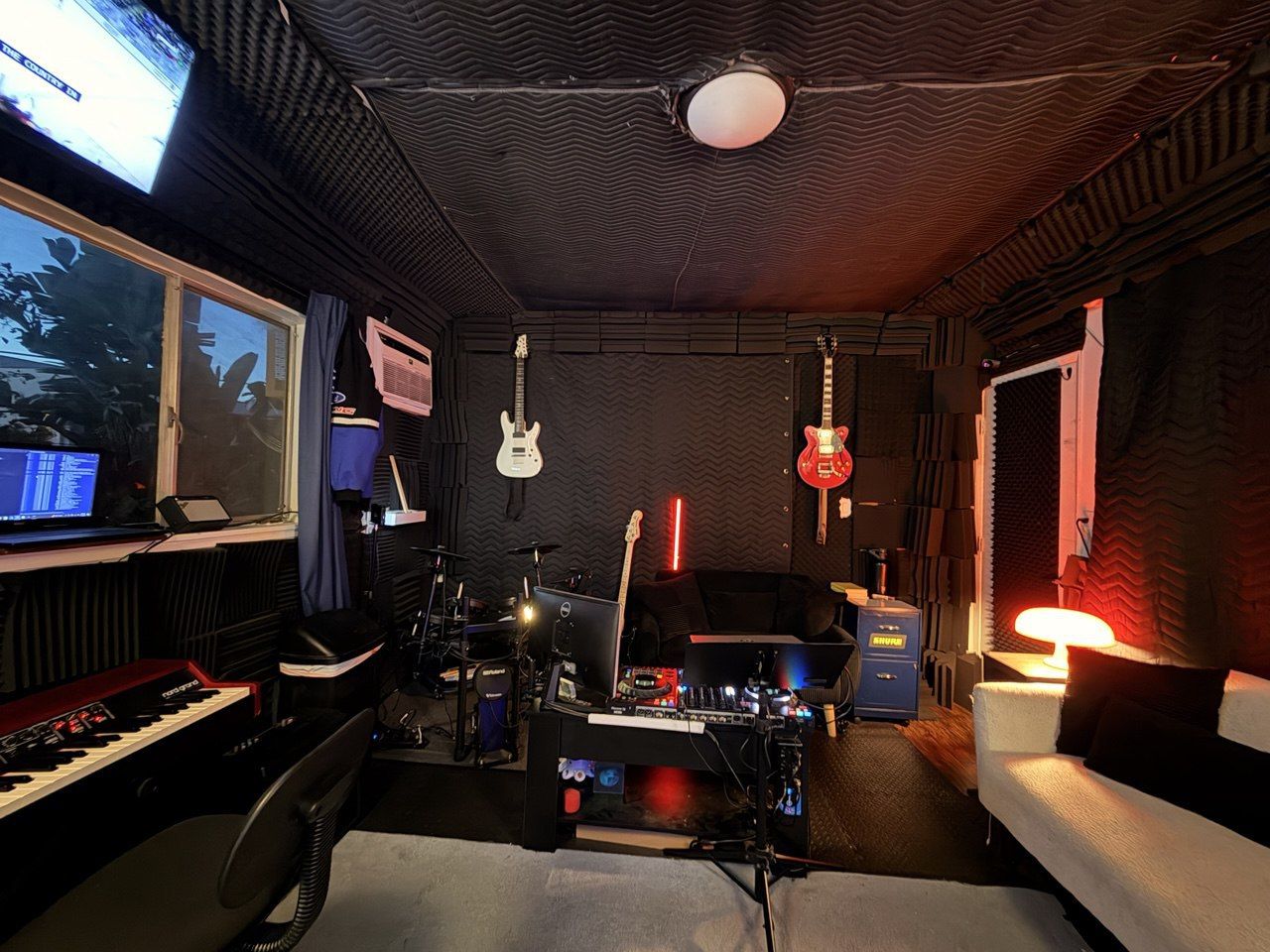 Guitar wall and back room — wall-mounted guitars, drums, red accent lighting, keyboard