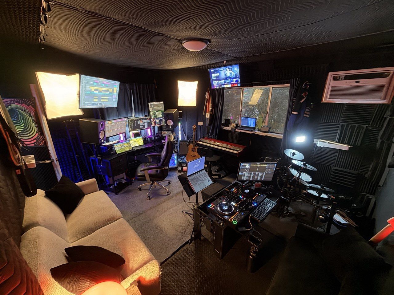 Full studio panorama — couch, DJ deck, drums, DAW screens, colorful psychedelic art